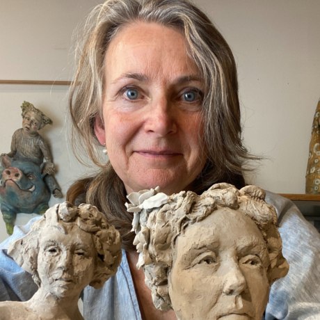 Artist Diane Black stands holding two sculptures of women